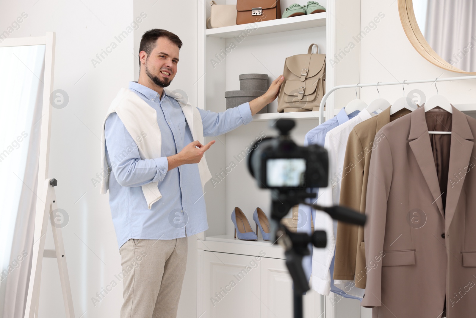 Photo of Smiling fashion blogger showing clothes while recording video at home