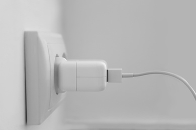 Charging adapter plugged in electric socket, closeup