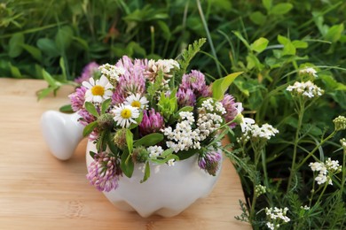 Ceramic mortar with pestle, different wildflowers and herbs on green grass outdoors