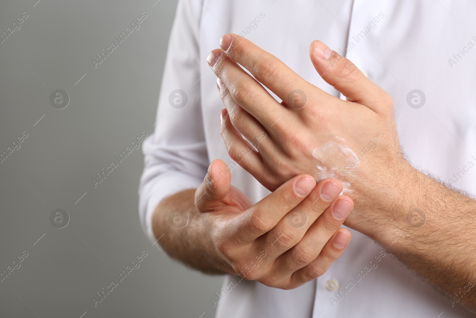 Photo of Man applying cream onto hand on grey background, closeup