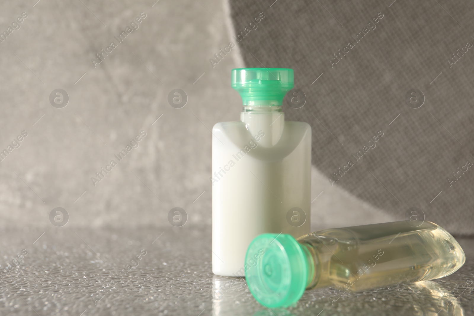 Photo of Mini bottles of cosmetic products on grey textured table, space for text