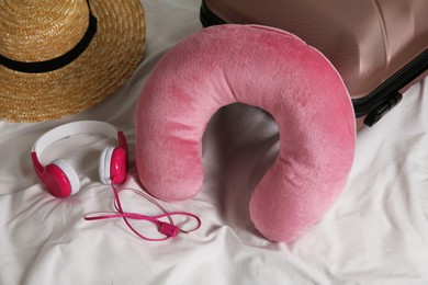 Photo of Pink travel pillow, suitcase, hat and headphones on bed