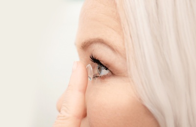 Photo of Senior woman putting contact lens in her eye indoors