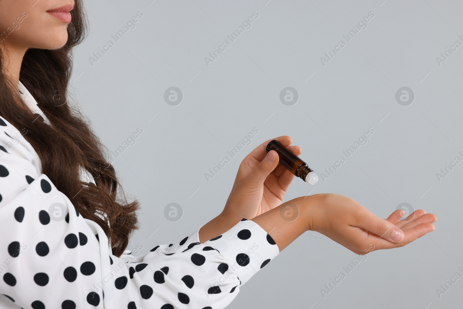 Photo of Woman with roller bottle applying essential oil onto wrist on light grey background, closeup