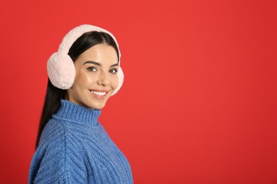 Photo of Beautiful young woman wearing earmuffs on red background. Space for text