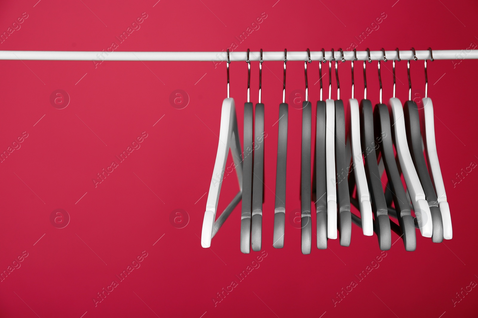 Photo of Empty clothes hangers on metal rail against color background. Space for text