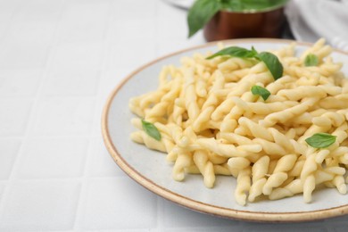 Plate of delicious trofie pasta with basil leaves on white tiled table, closeup. Space for text