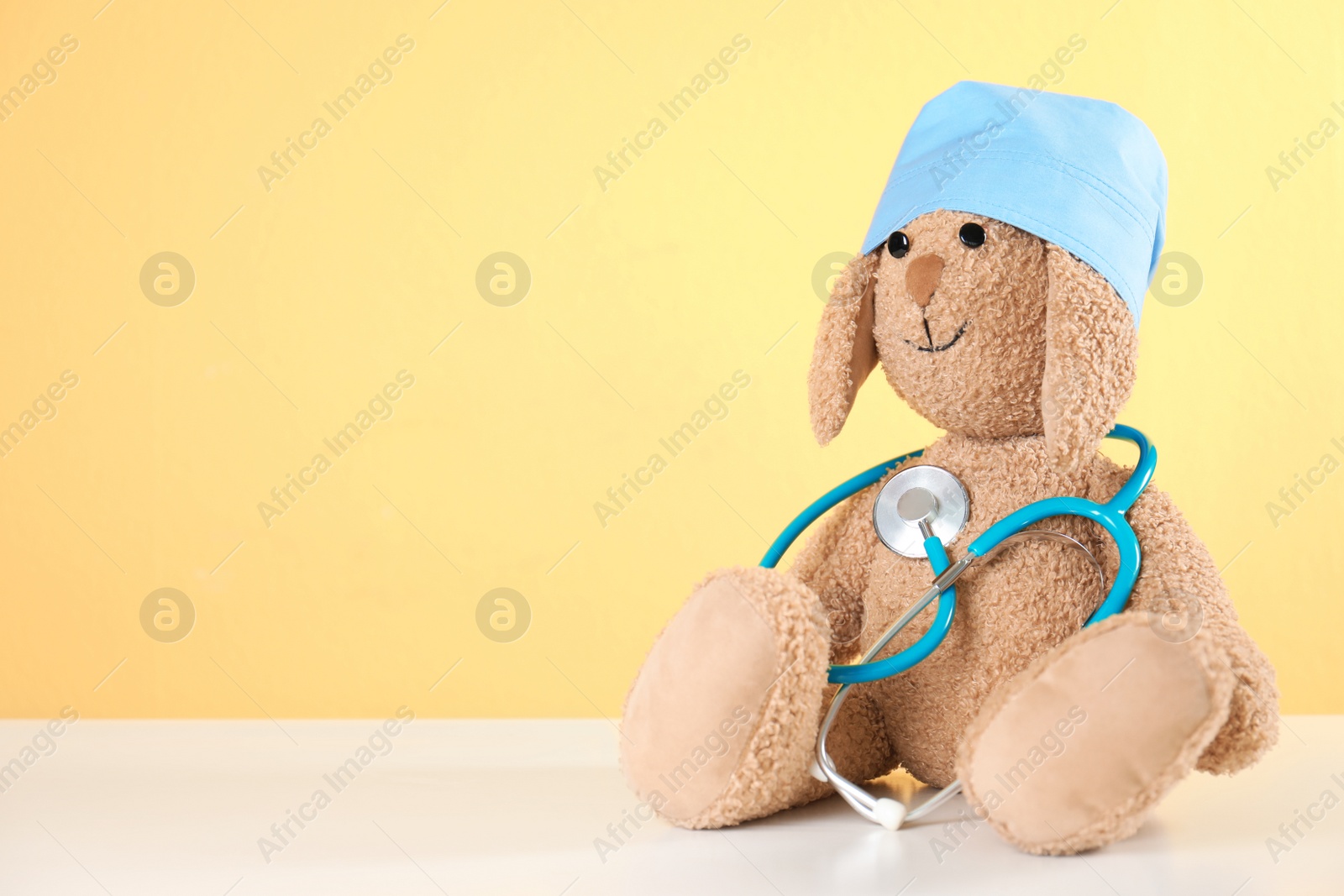 Photo of Toy bunny with stethoscope on table against color background, space for text. Children's hospital