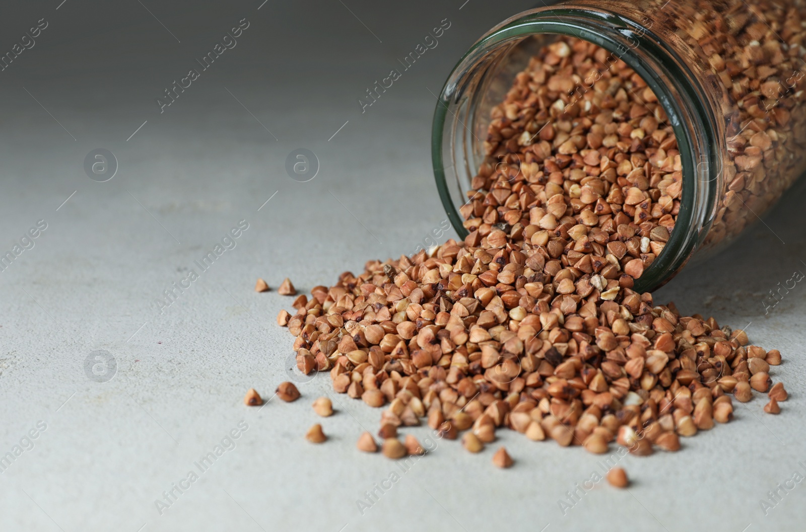 Photo of Uncooked organic buckwheat grains on light grey table. Space for text