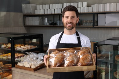 Photo of Happy seller holding tray with tasty croissants in bakery shop