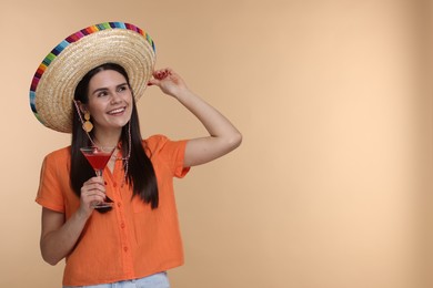 Photo of Young woman in Mexican sombrero hat with cocktail on beige background. Space for text