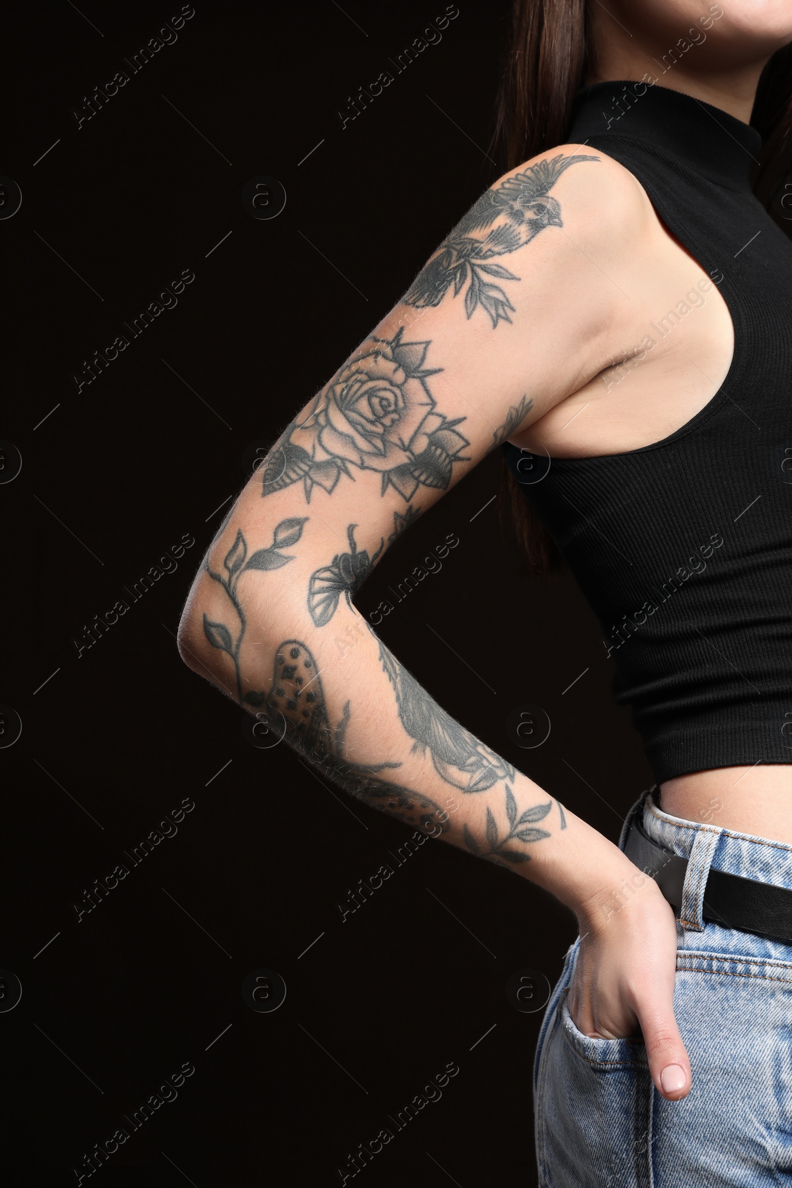 Photo of Beautiful woman with tattoos on arm against black background, closeup