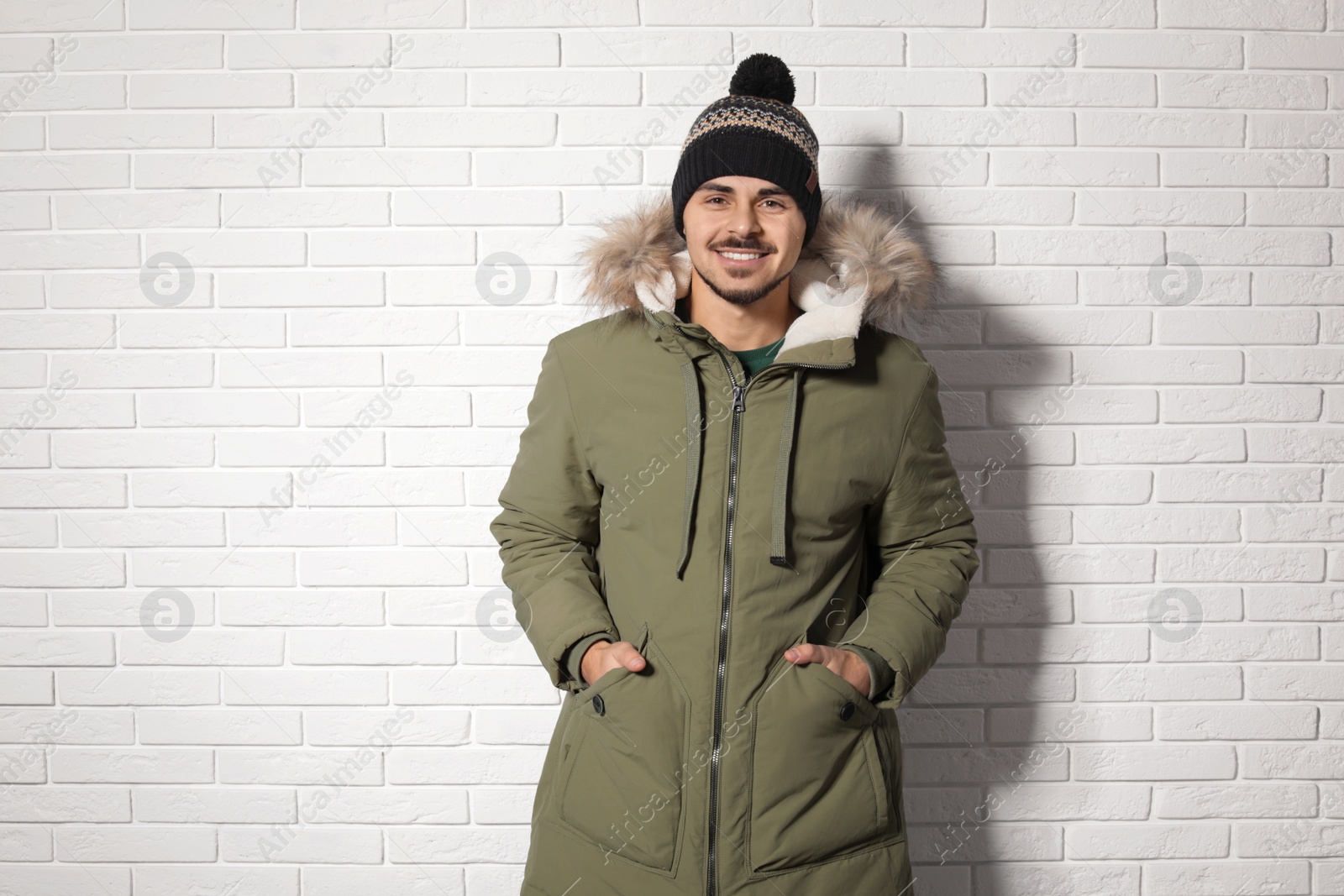 Photo of Young man wearing warm clothes against brick wall. Ready for winter vacation