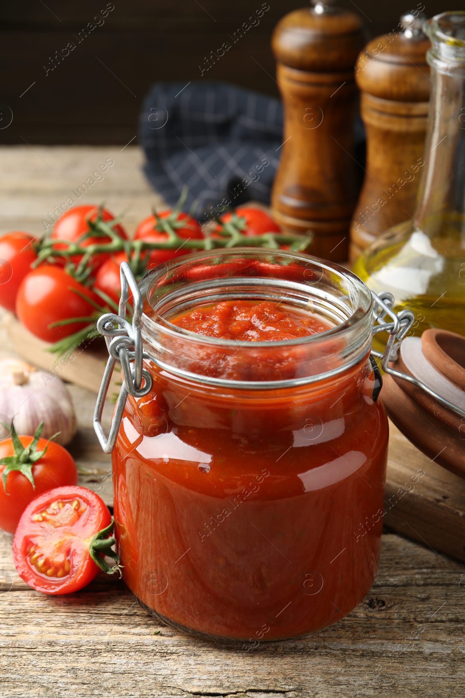 Photo of Homemade tomato sauce in jar and fresh ingredients on wooden table, closeup