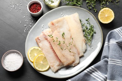 Photo of Raw cod fish, microgreens, lemon and spices on dark table, flat lay