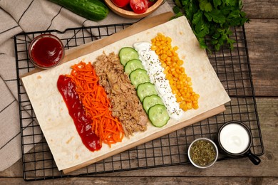 Delicious tortilla with tuna, vegetables and sauces on wooden table, flat lay. Cooking shawarma