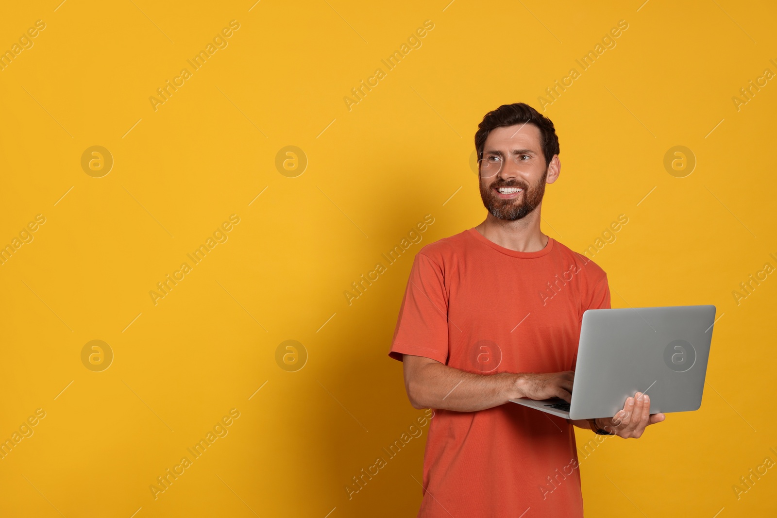 Photo of Handsome man with laptop on orange background. Space for text