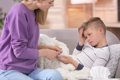 Mother taking care of little son suffering from cold on sofa