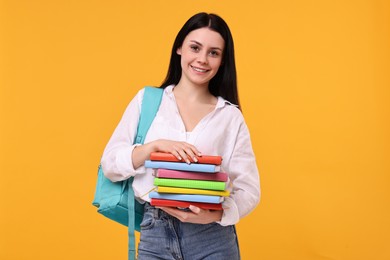 Smiling student with stack of books on yellow background