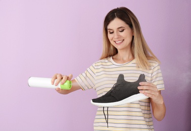 Photo of Woman spraying air freshener on shoe against color background