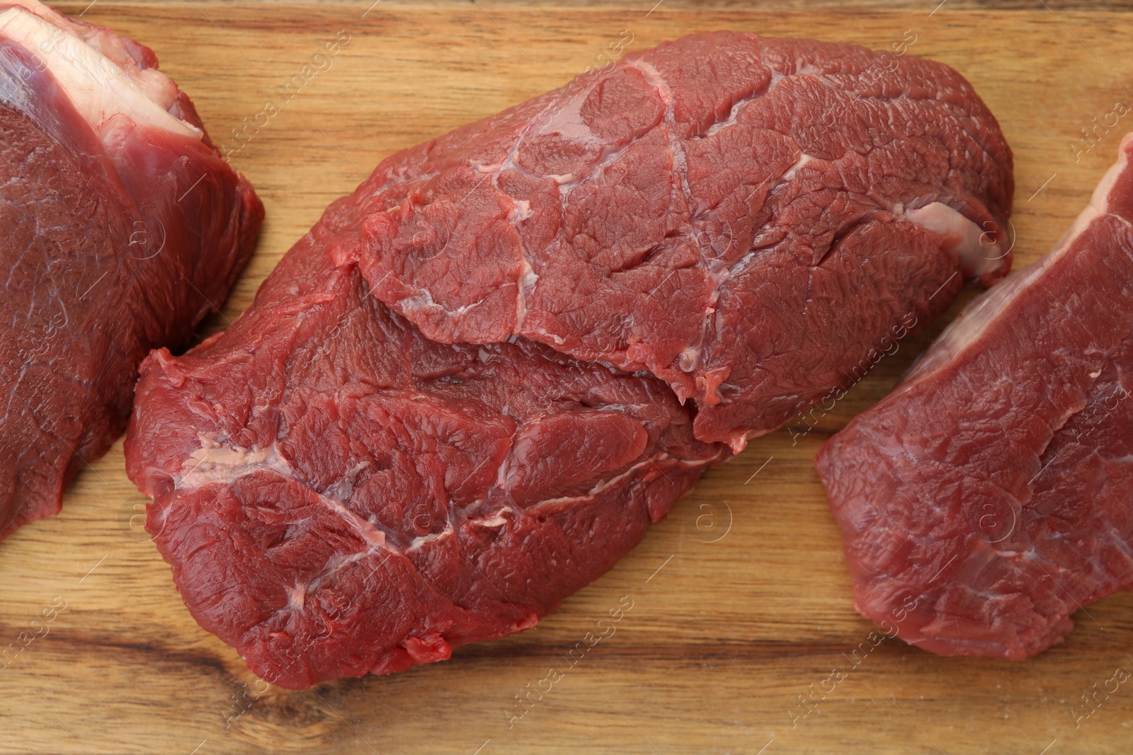 Photo of Pieces of raw beef meat on wooden table, top view