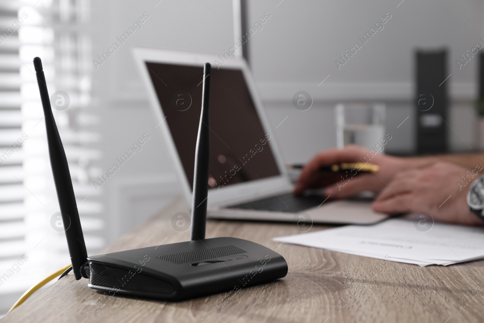 Photo of Man working with laptop in office, focus on connected router. Wireless internet communication