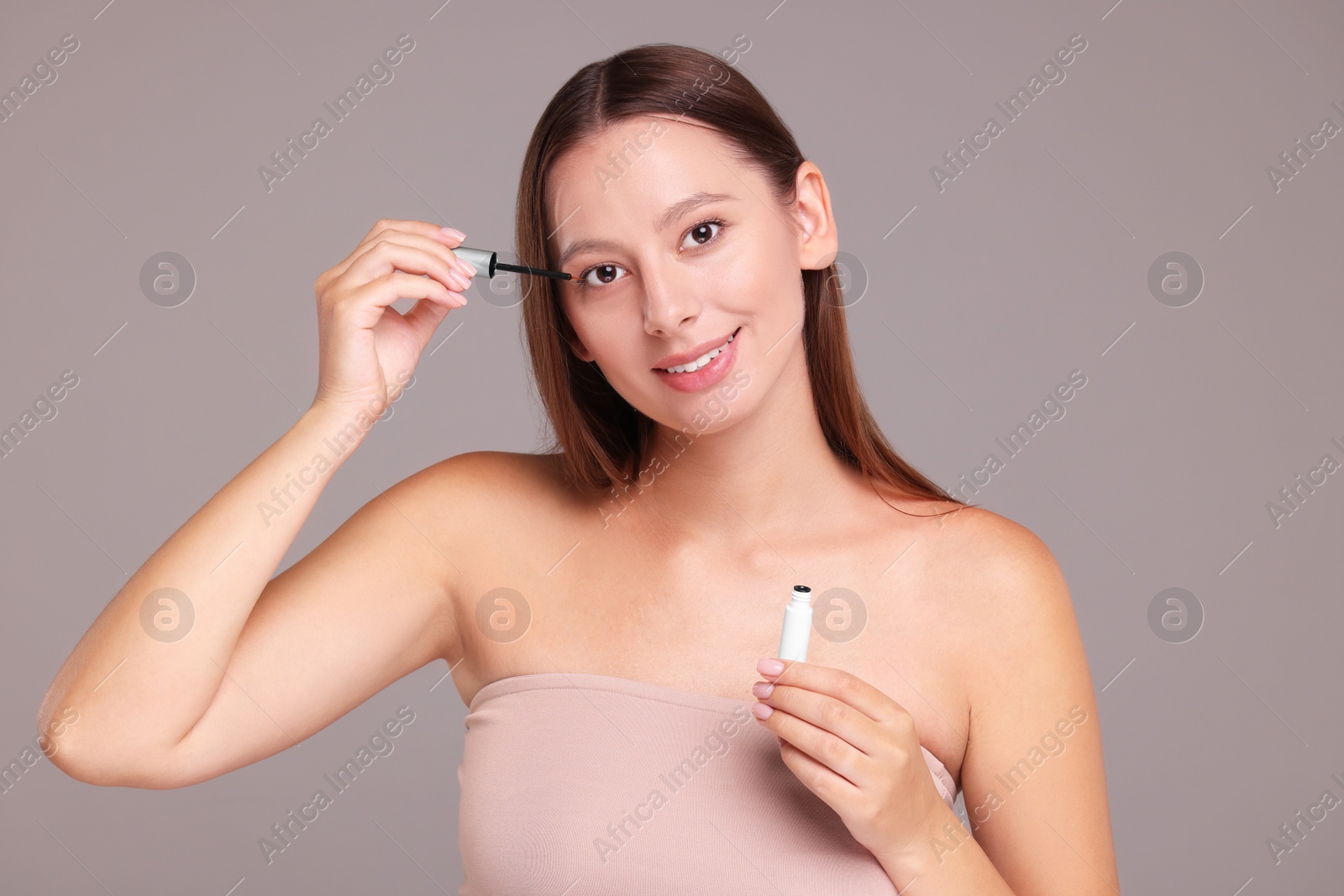 Photo of Beautiful woman applying serum onto eyelashes on grey background