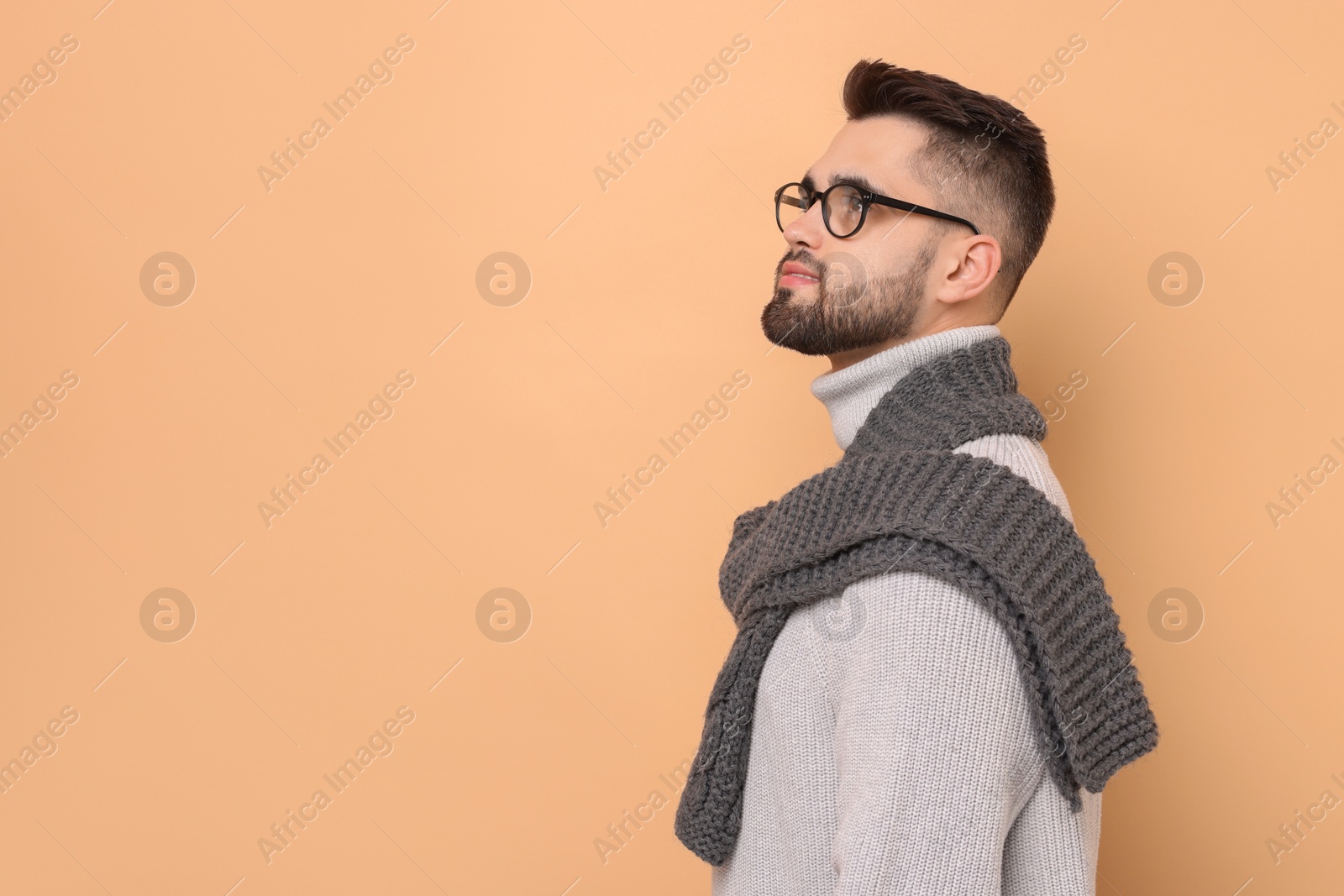 Photo of Handsome man in knitted scarf on beige background. Space for text