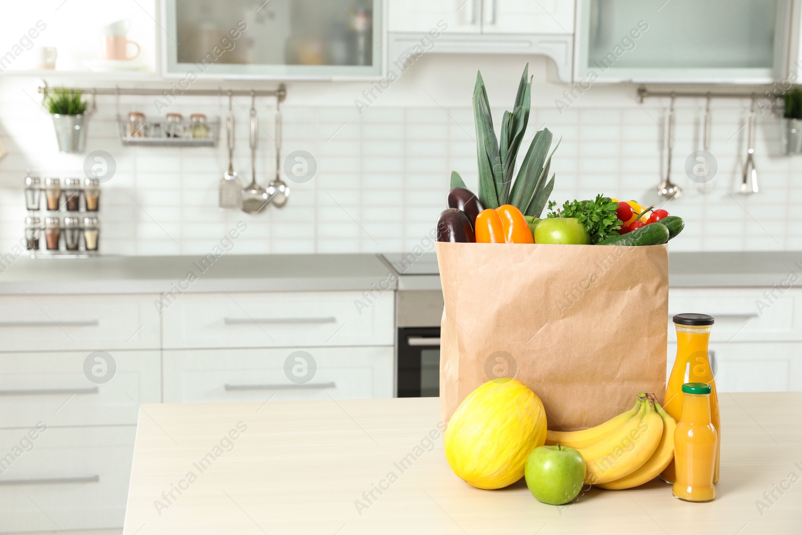 Photo of Paper shopping bag full of vegetables with fruits and juice on table in kitchen. Space for text