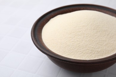 Photo of Uncooked organic semolina in bowl on white tiled table, closeup. Space for text