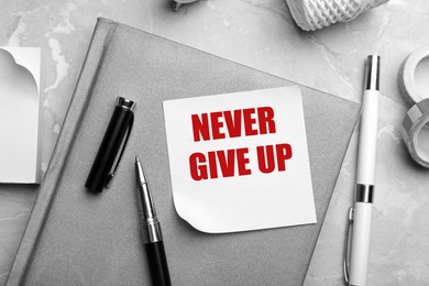 Image of Note with phrase Never Give Up and stationery on table, flat lay