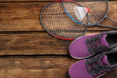 Rackets, shuttlecock and shoes on wooden table, flat lay with space for text. Playing badminton