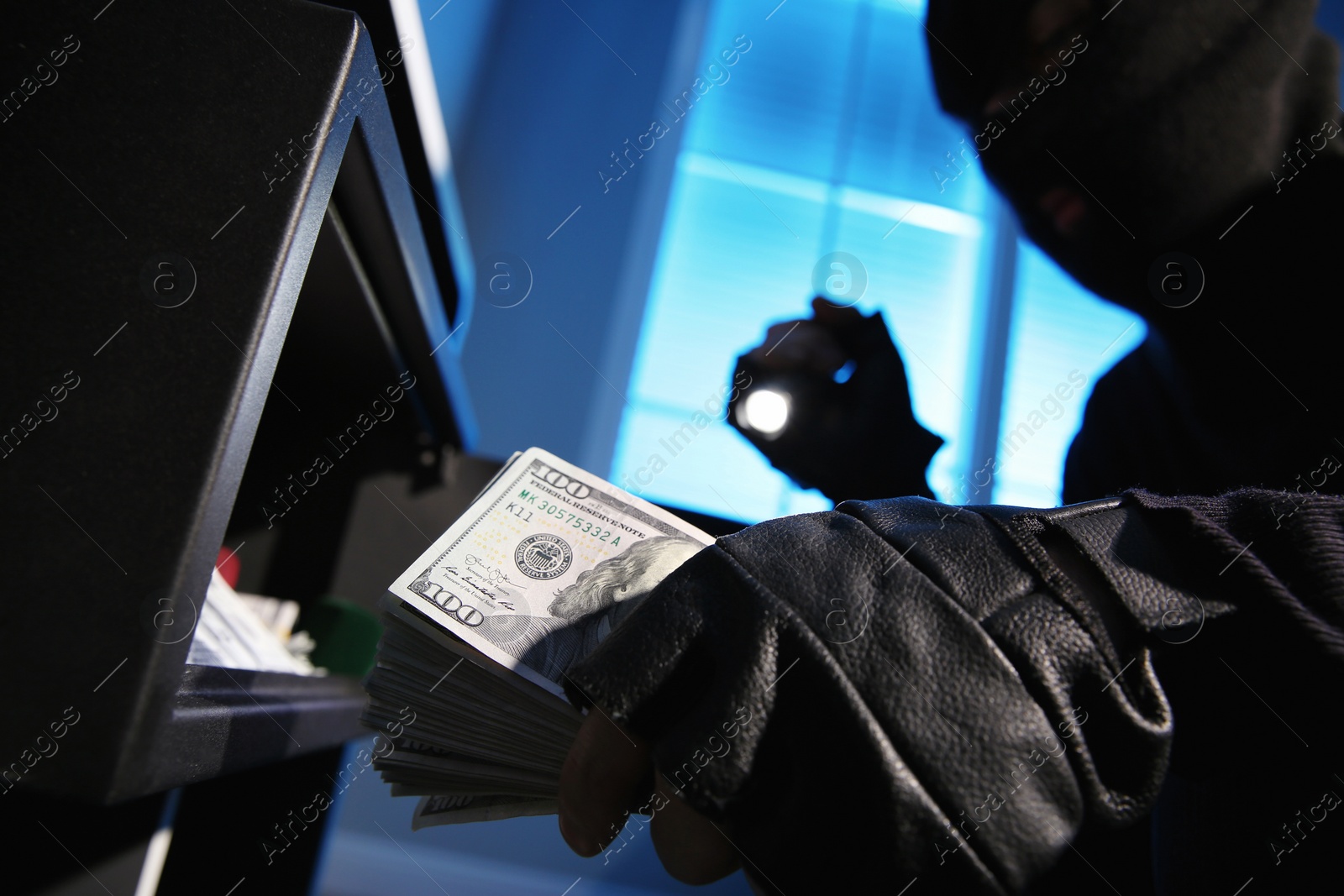 Photo of Thief taking money out of steel safe indoors at night, closeup