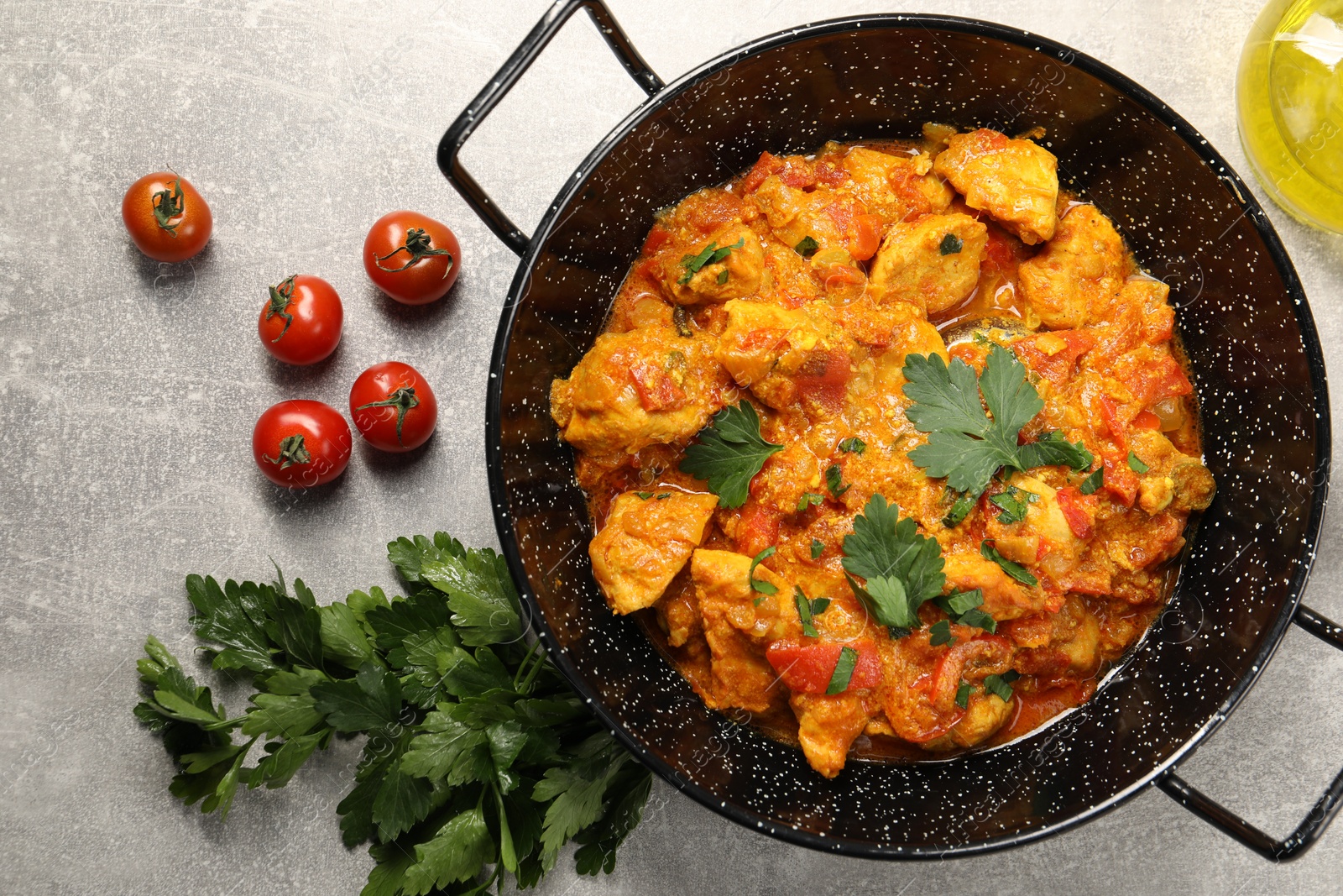 Photo of Delicious chicken curry in frying pan, parsley and tomatoes on light grey table, flat lay