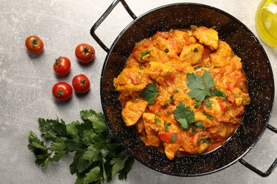 Photo of Delicious chicken curry in frying pan, parsley and tomatoes on light grey table, flat lay