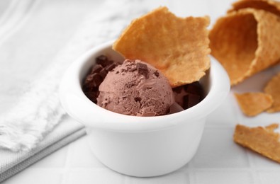 Tasty chocolate ice cream and piece of waffle cone in bowl on white table, closeup