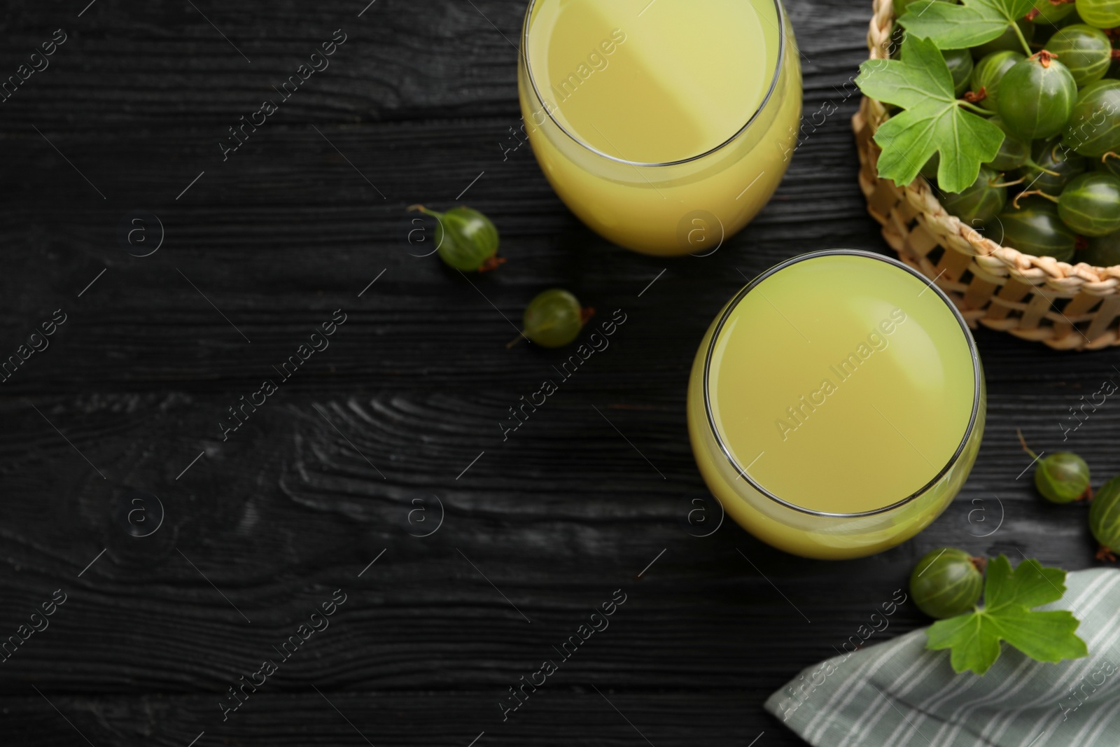 Photo of Tasty gooseberry juice on black wooden table, flat lay. Space for text