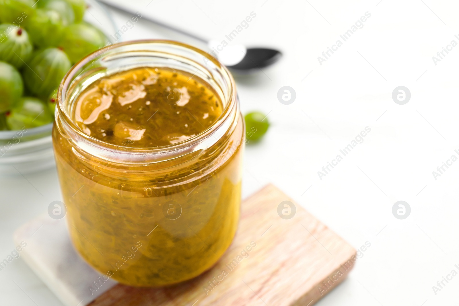 Photo of Jar of delicious gooseberry jam and fresh berries on white table, closeup. Space for text