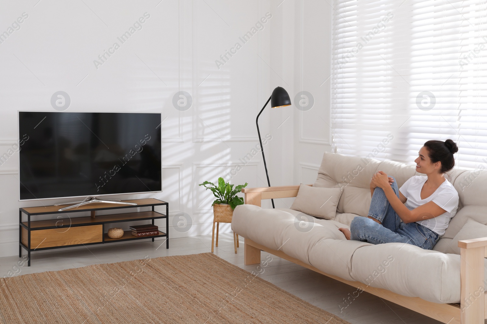 Photo of Woman watching television at home. Living room interior with TV on stand