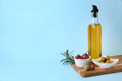 Photo of Bottle of oil, olives and tree twig on light blue background, space for text