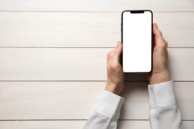 Woman with smartphone at white wooden table, top view. Space for text