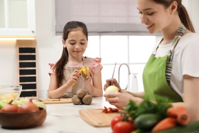 Photo of Mother and daughter peeling vegetables at table in kitchen