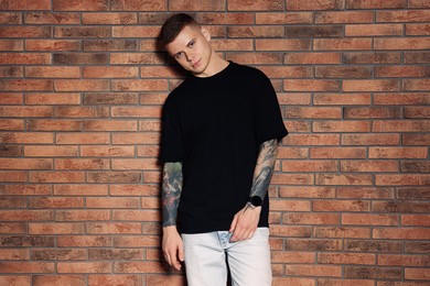 Photo of Young man with tattoos near brick wall
