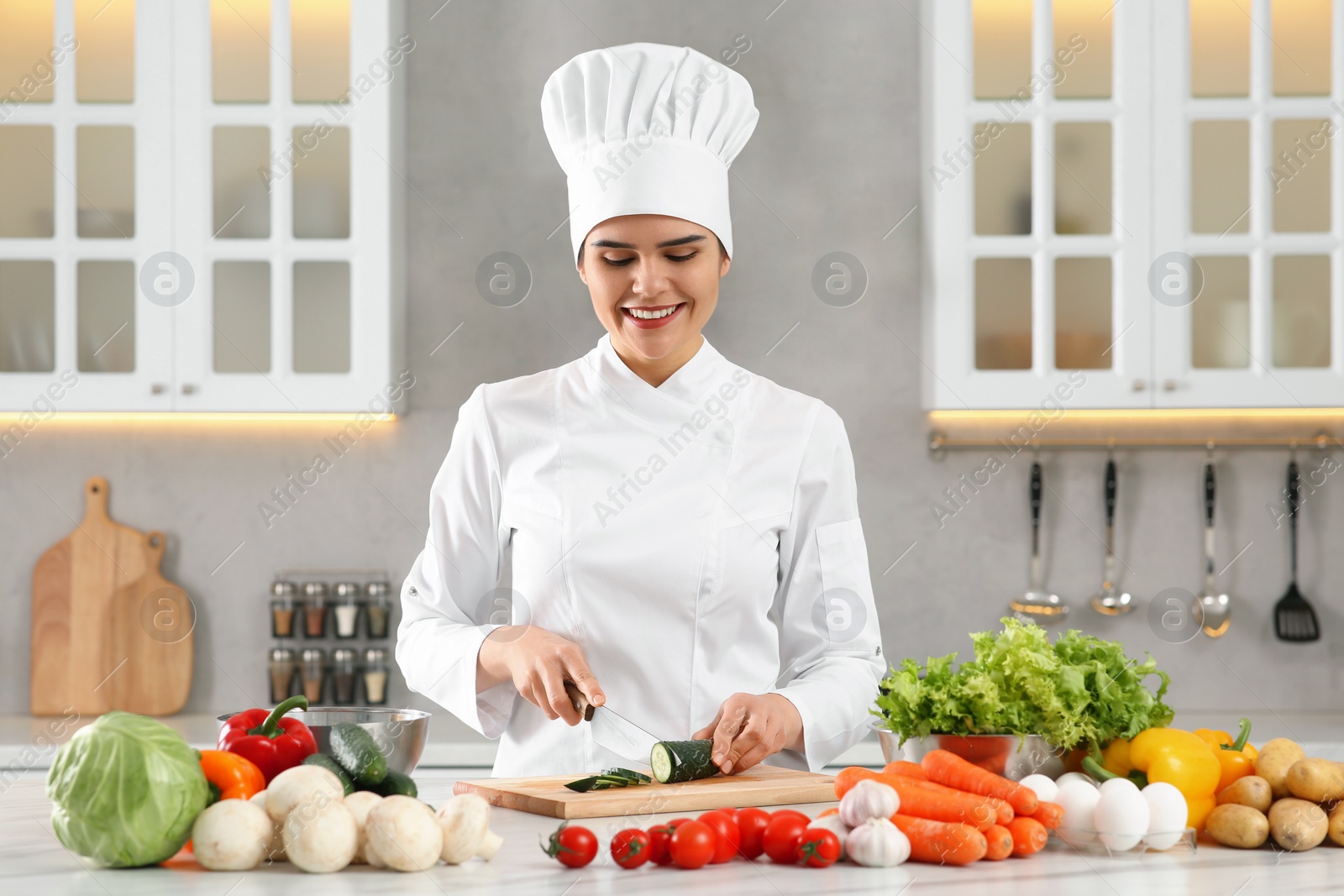 Photo of Professional chef cutting fresh cucumber at white table in kitchen