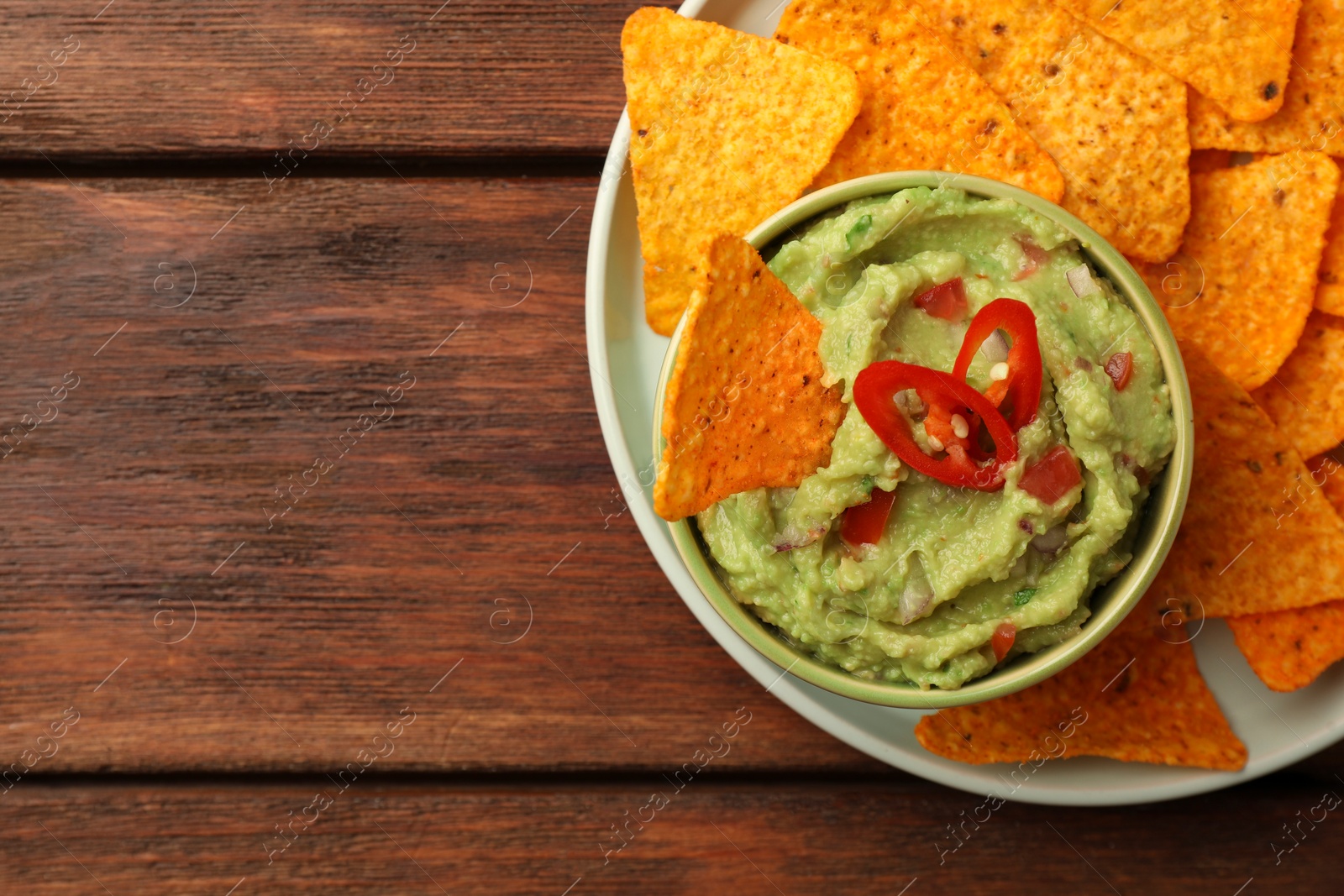 Photo of Bowl of delicious guacamole and nachos chips on wooden table, top view. Space for text