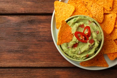 Bowl of delicious guacamole and nachos chips on wooden table, top view. Space for text