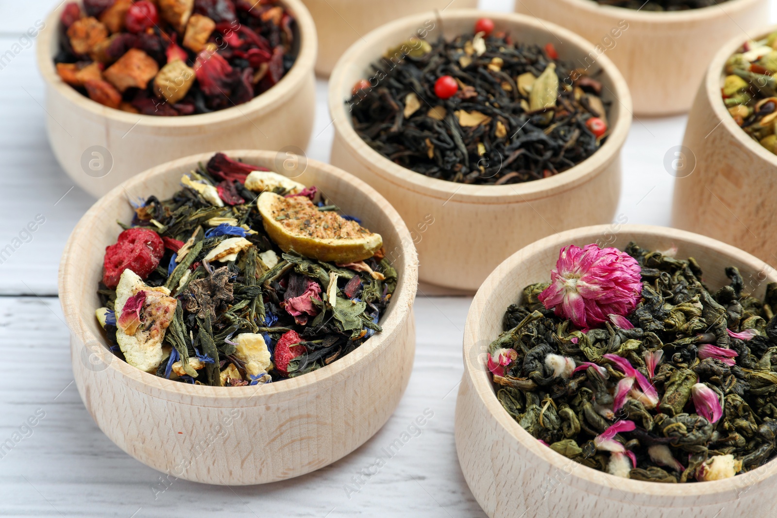 Photo of Different kinds of dry herbal tea in bowls on white wooden table