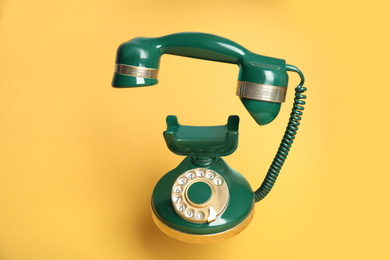 Green vintage corded phone on yellow background