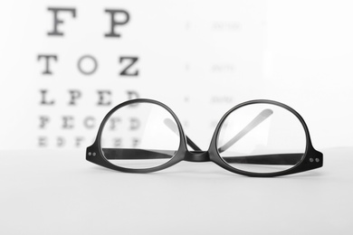 Photo of Glasses with corrective lenses on table against eye chart