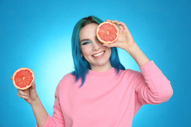 Photo of Young woman with bright dyed hair holding grapefruit on light blue background